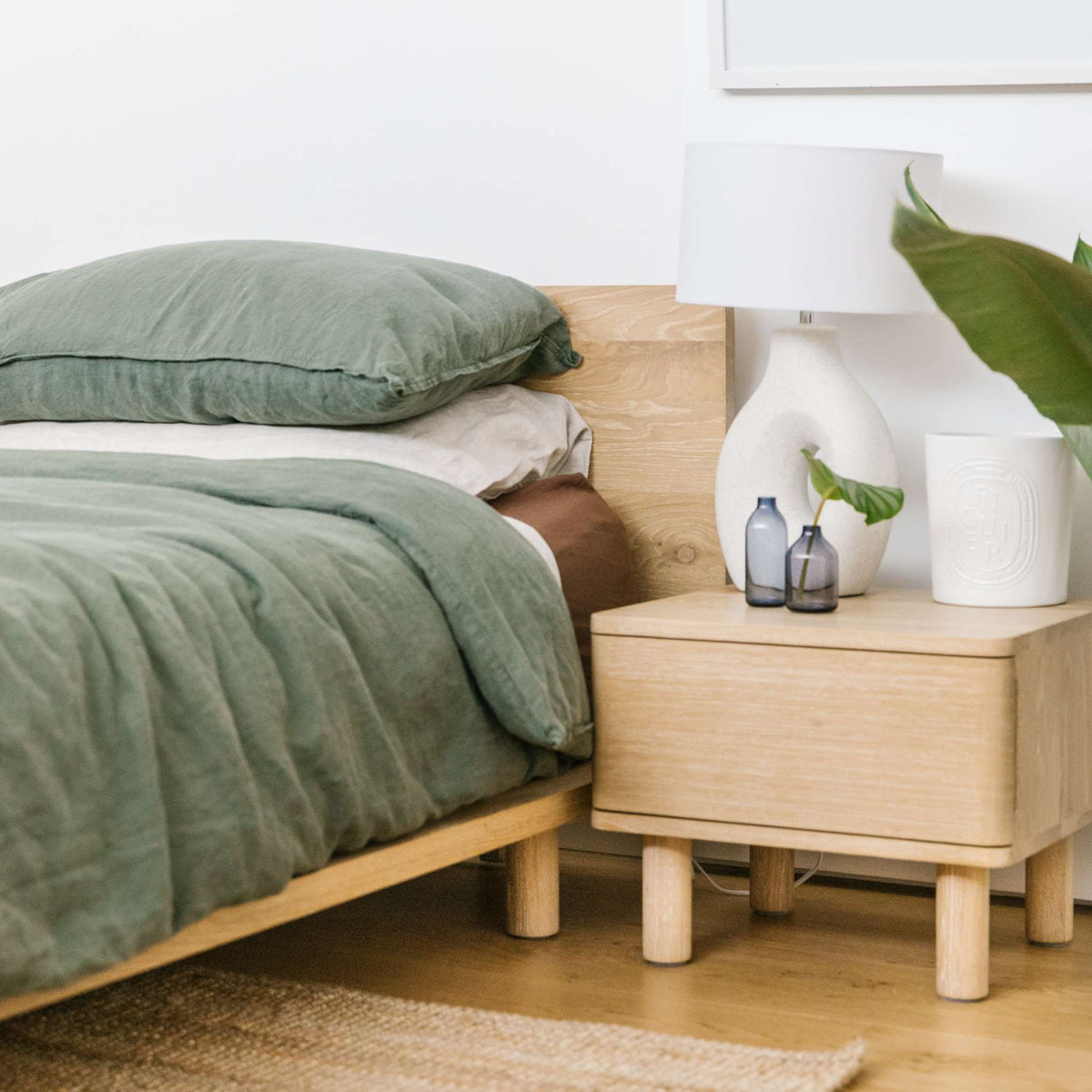 Lagos timber bed frame in solid oak styled with green linen bedding and matching oak bedside table – Totem Road